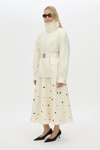 Side styled view CAMILLA AND MARC Drea funnel neck puffer jacket in cream with utility waistbelt and detachable throat latch.