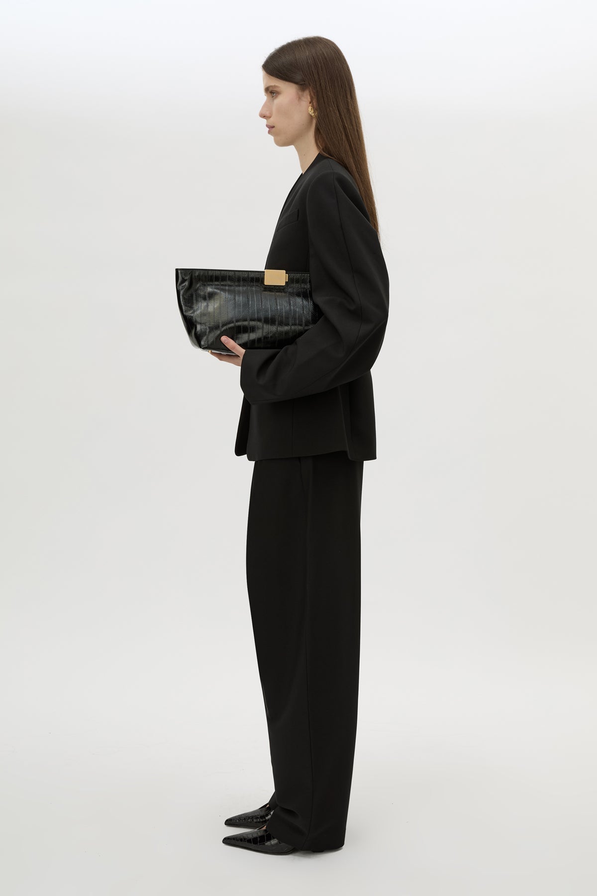 Front styled view CAMILLA AND MARC Poppy Eel Clutch in Black eel‑embossed leather with ribbed gold hardware.